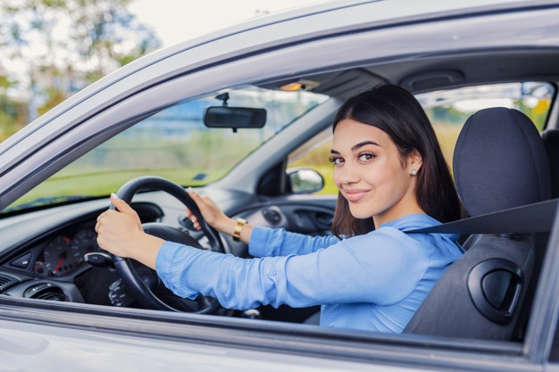mulher com as duas mãos no volante de um carro olhando para a janela lateral do veículo