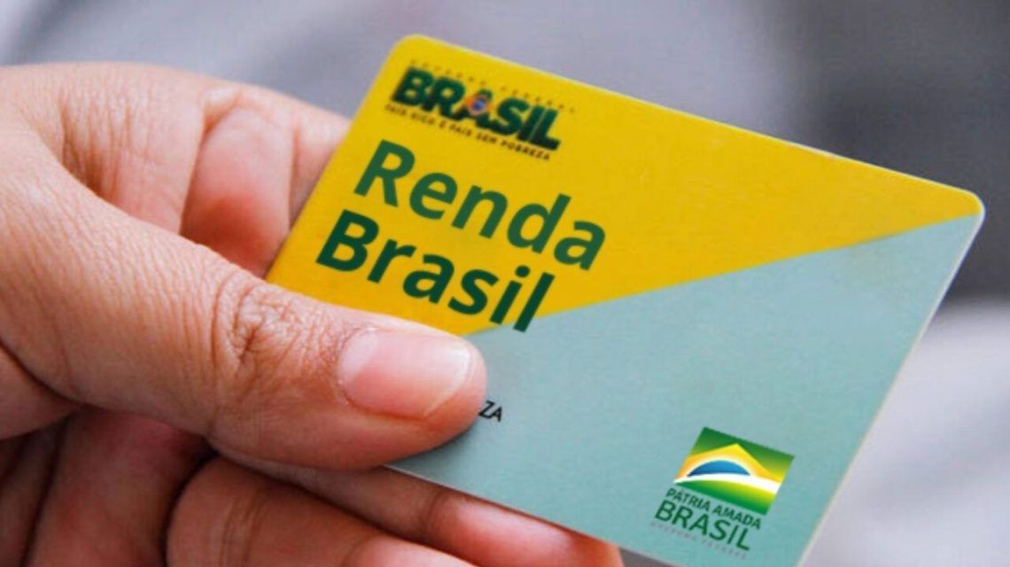 mão segurando um cartão escrito Renda Brasil nas cores amarelo, verde e azul claro